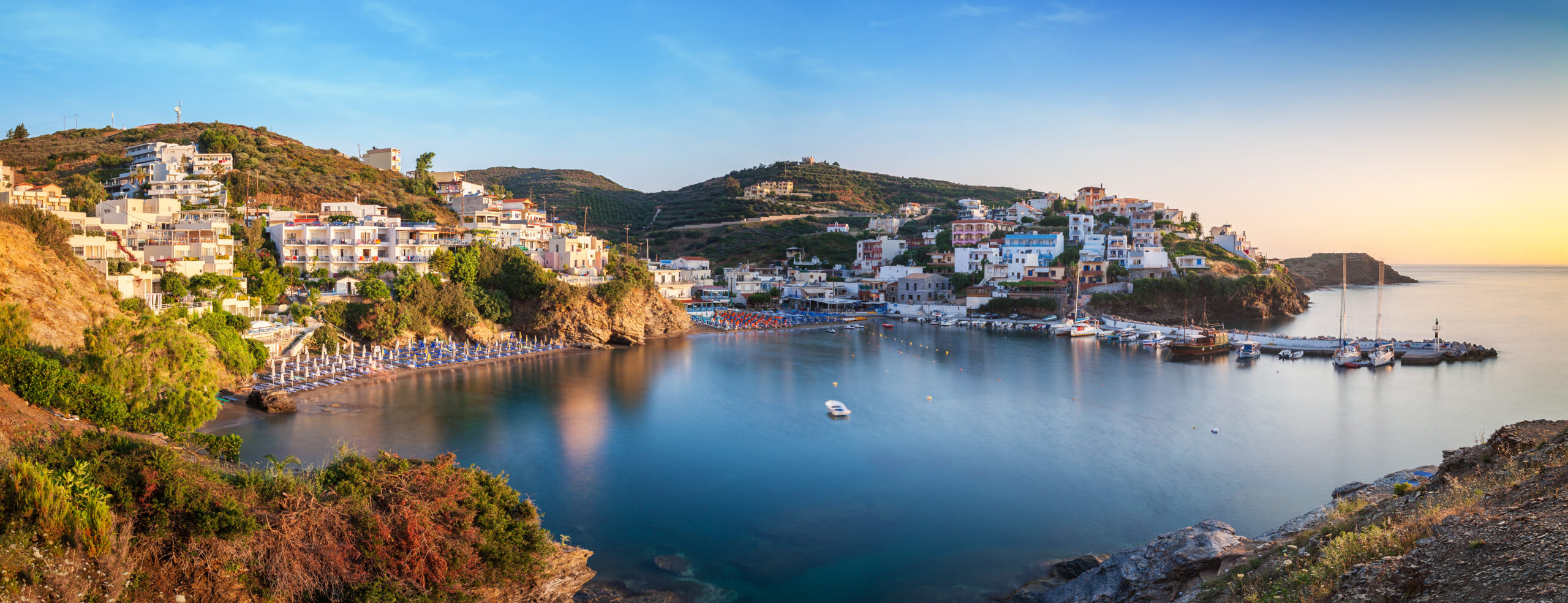 panorama of harbour with vessels, boats, beach and lighthouse in bali at sunrise, crete, greece